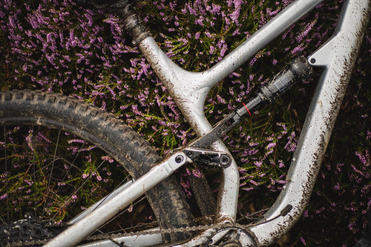 Muddy full-suspension mountain bike frame with a RockShox rear shock, lying in heather.