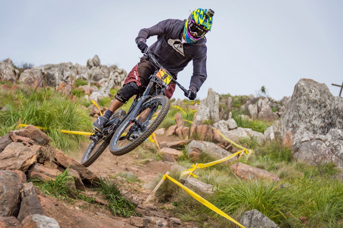 Downhill rider in a full-face helmet picking through a rocky alpine trail on a full-suspension bike.