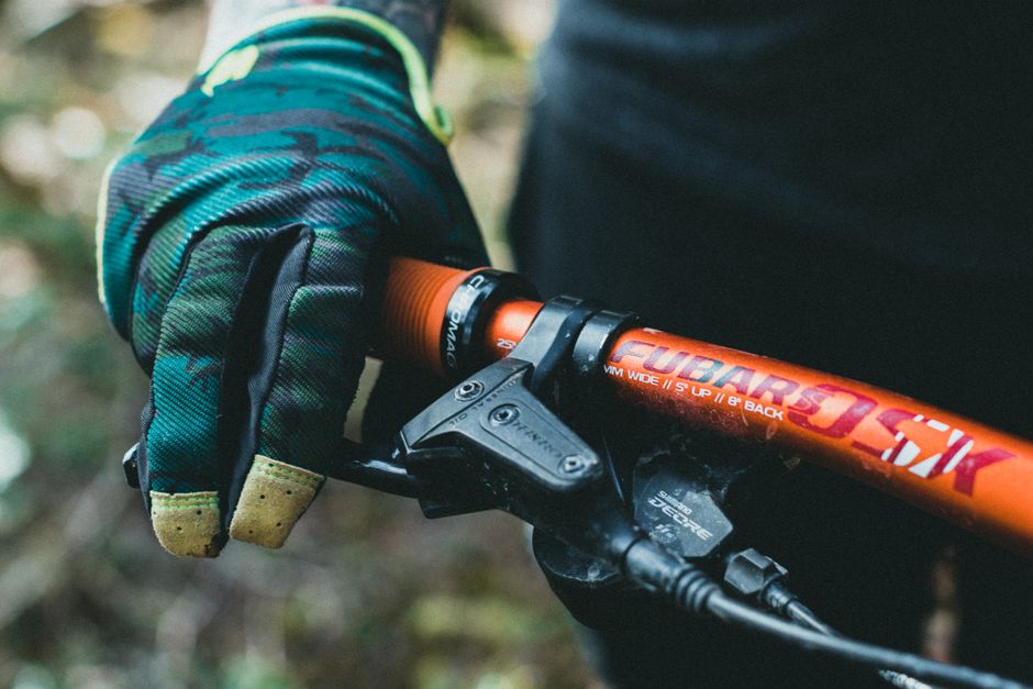 Gloved hand on a lock-on grip with a single inboard clamp, on an alloy handlebar with a Shimano brake lever.