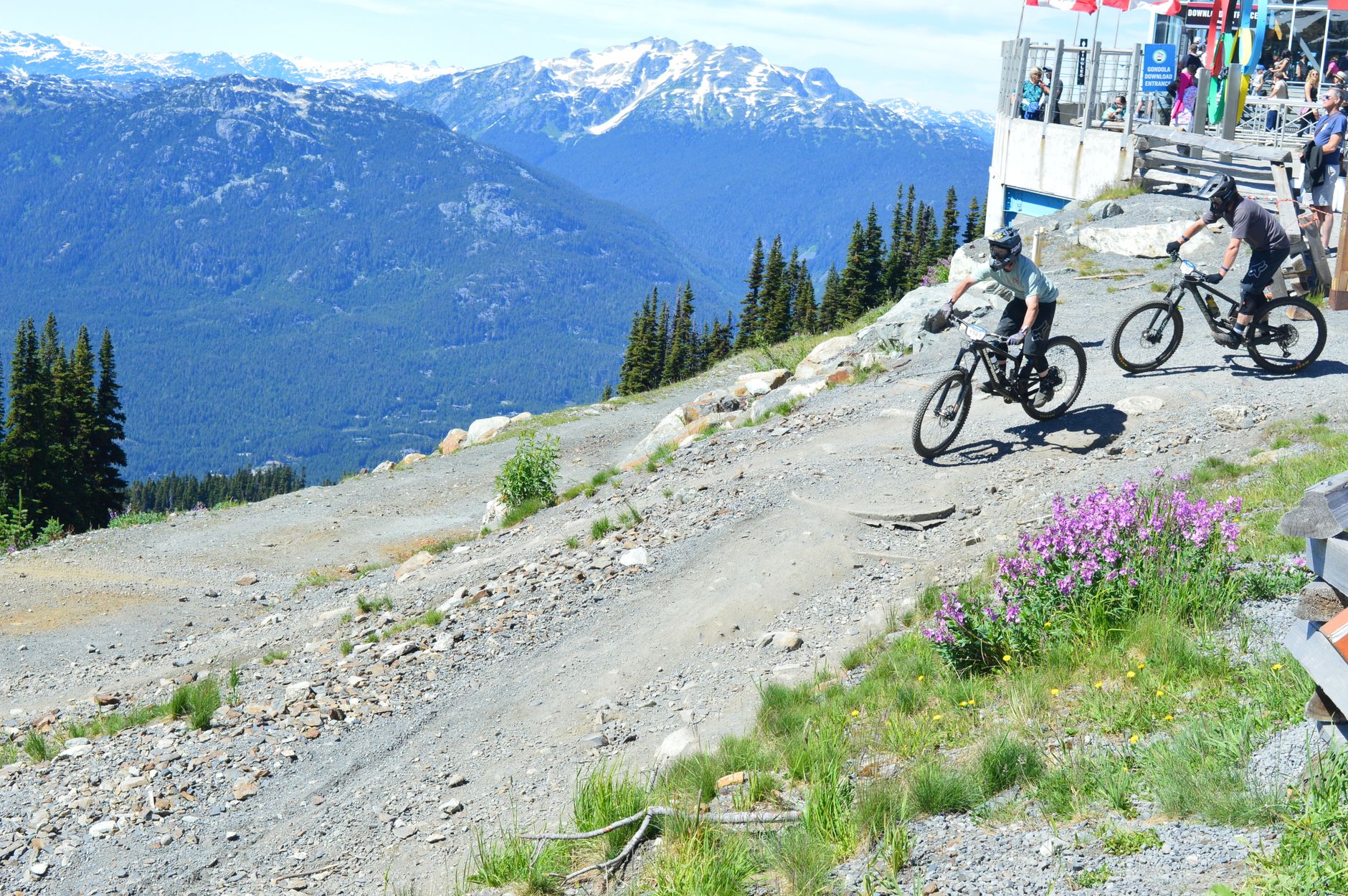 Two riders on full-suspension mountain bikes dropping into a loose, rocky alpine trail at the top of the Whistler bike park.
