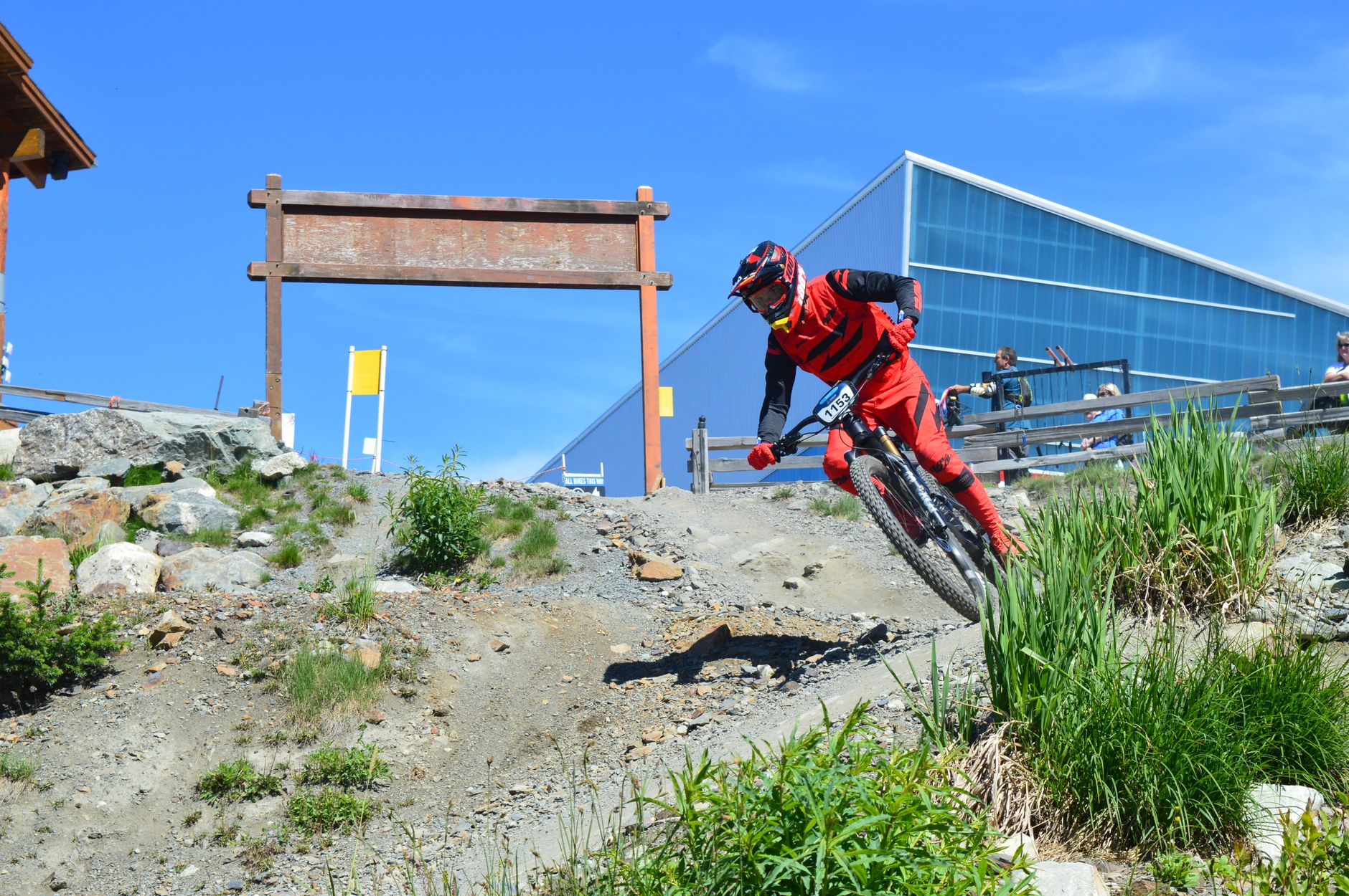 Downhill racer in red kit leaning a downhill bike into a gravel corner at a race in Whistler, British Columbia.