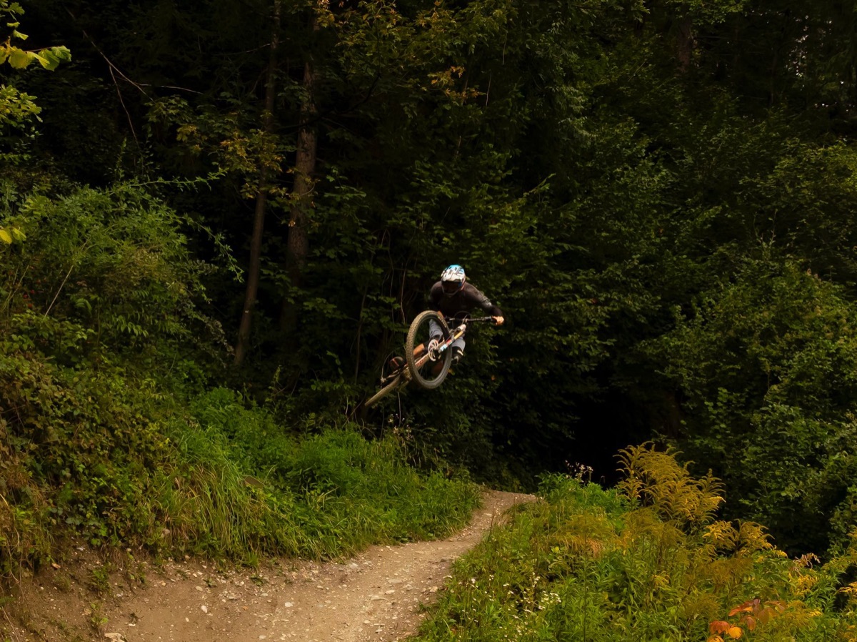 Mountain biker catching air on a forest trail, suspension fully loaded.