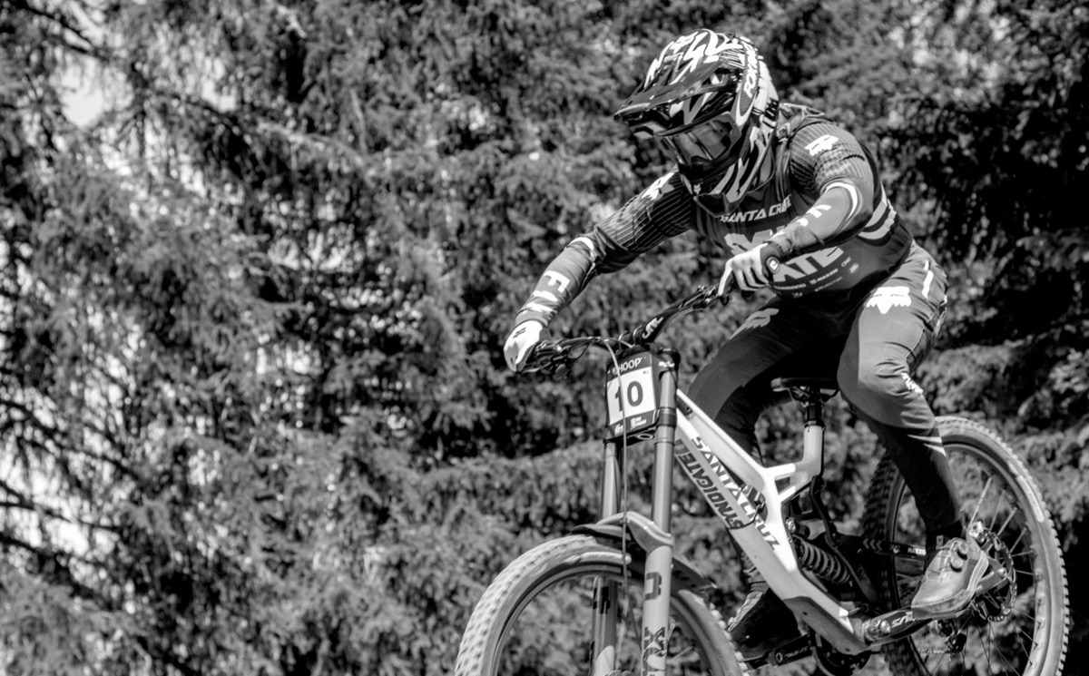 Black-and-white DH race shot of a Santa Cruz downhill bike mid-air, Fox 40 fork and RockShox rear coil.