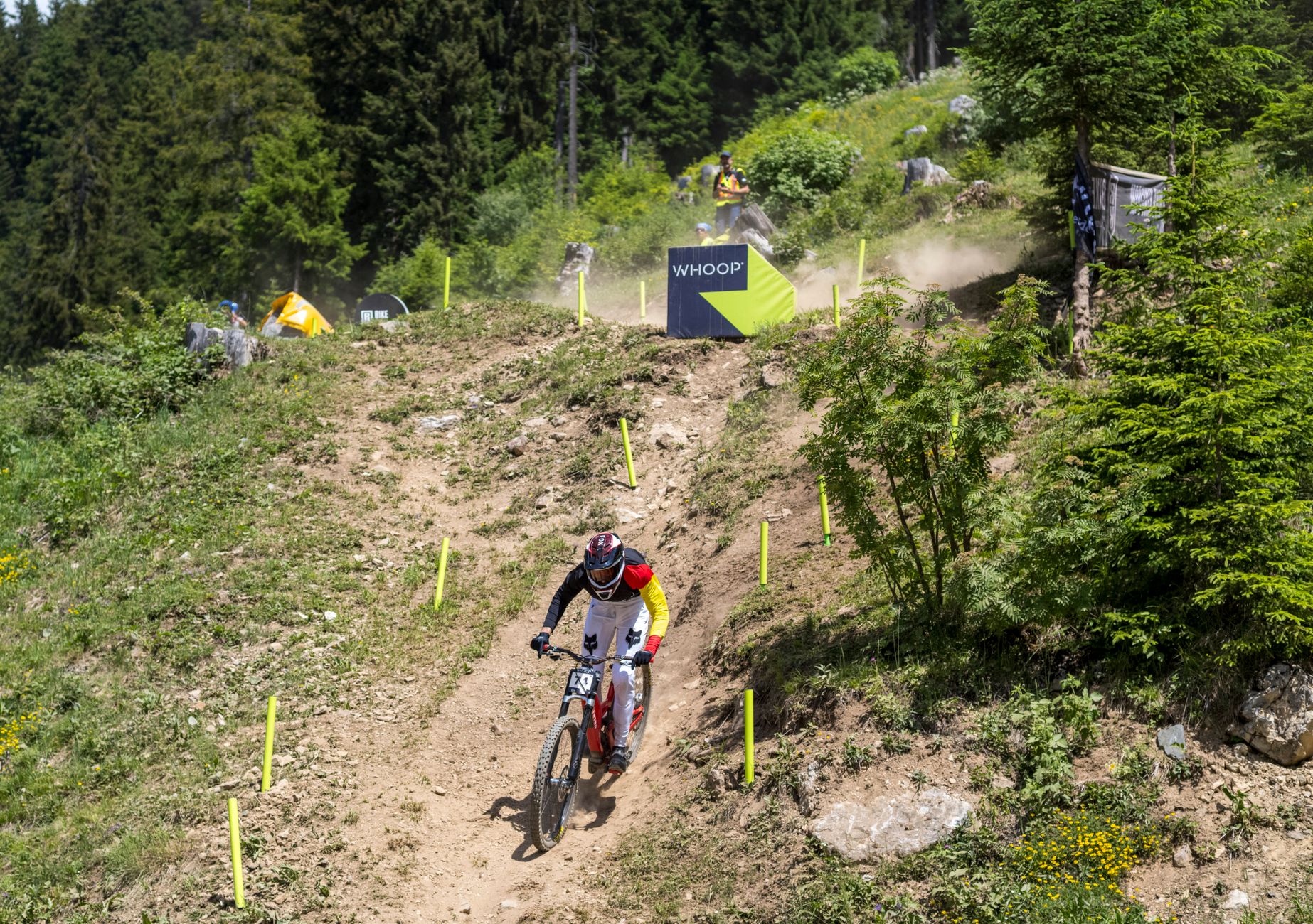 Downhill racer in a full-face helmet riding down a steep, dusty chute between course markers in Switzerland.