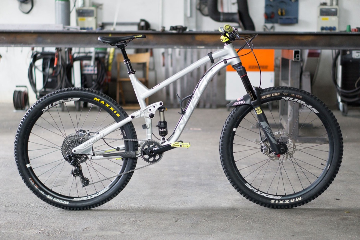 Full-suspension trail mountain bike on a workshop bench, complete with fork, rear shock, drivetrain and wheels.
