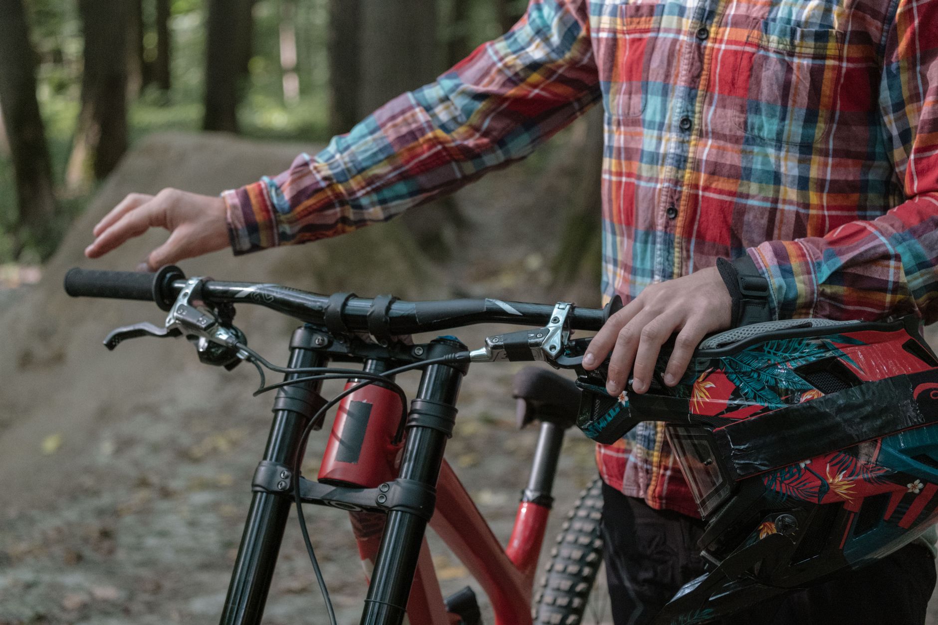 Rider standing behind a mountain bike with both hands on a wide handlebar, brake levers and grips in view.